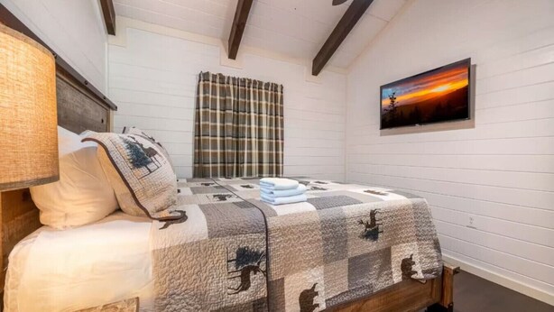 A bedroom with a bed, a window with curtains, a painting on the wall, and a wooden ceiling beam. - Rustic 2BR Farm Cabin: Hot Tub, Animals & Hiking (Sevierville)