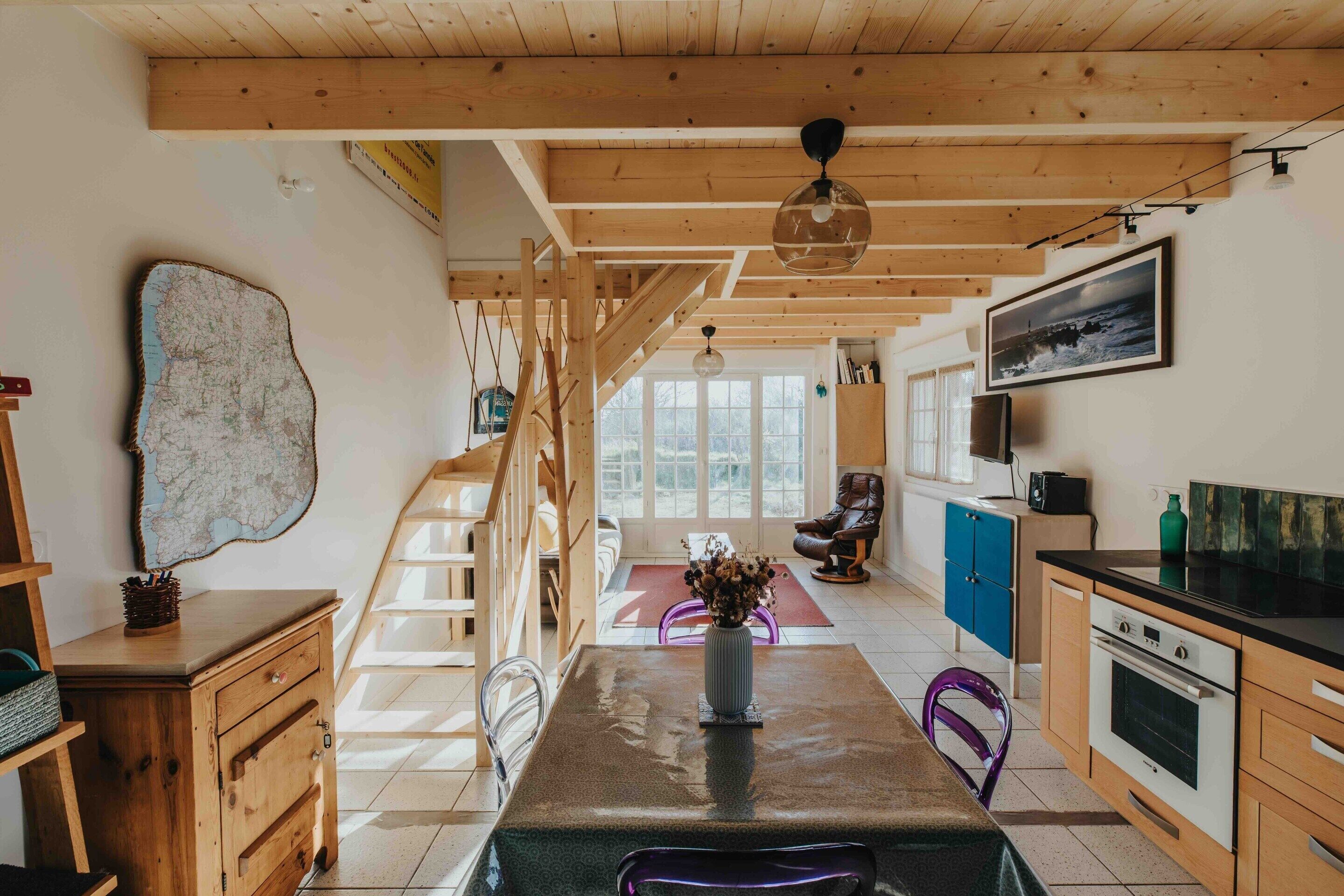 A spacious kitchen with wooden beams, a dining area with a table and chairs, and a staircase leading to another level.
