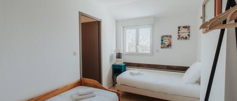 A room with two beds, a window, a door, and a wall-mounted rack.
