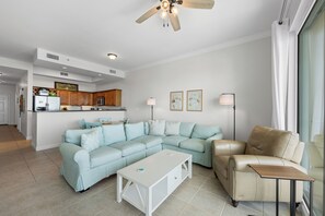 Una sala moderna con un sofá seccional, una mesa de centro, un sillón de cuero y un comedor con armarios de madera y un refrigerador.