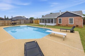 Un jardin avec une piscine, une terrasse couverte et une maison en briques.