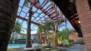 A pool area with a wooden pergola, palm trees, and a brick building. - House with pool in Praia Grande with 2 Wi-Fi networks in the house, comfortably accommodates up to 20 people!! (Praia Grande)
