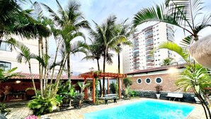 A swimming pool surrounded by palm trees and a brick building with a red roof. - House with pool in Praia Grande with 2 Wi-Fi networks in the house, comfortably accommodates up to 20 people!! (Praia Grande)