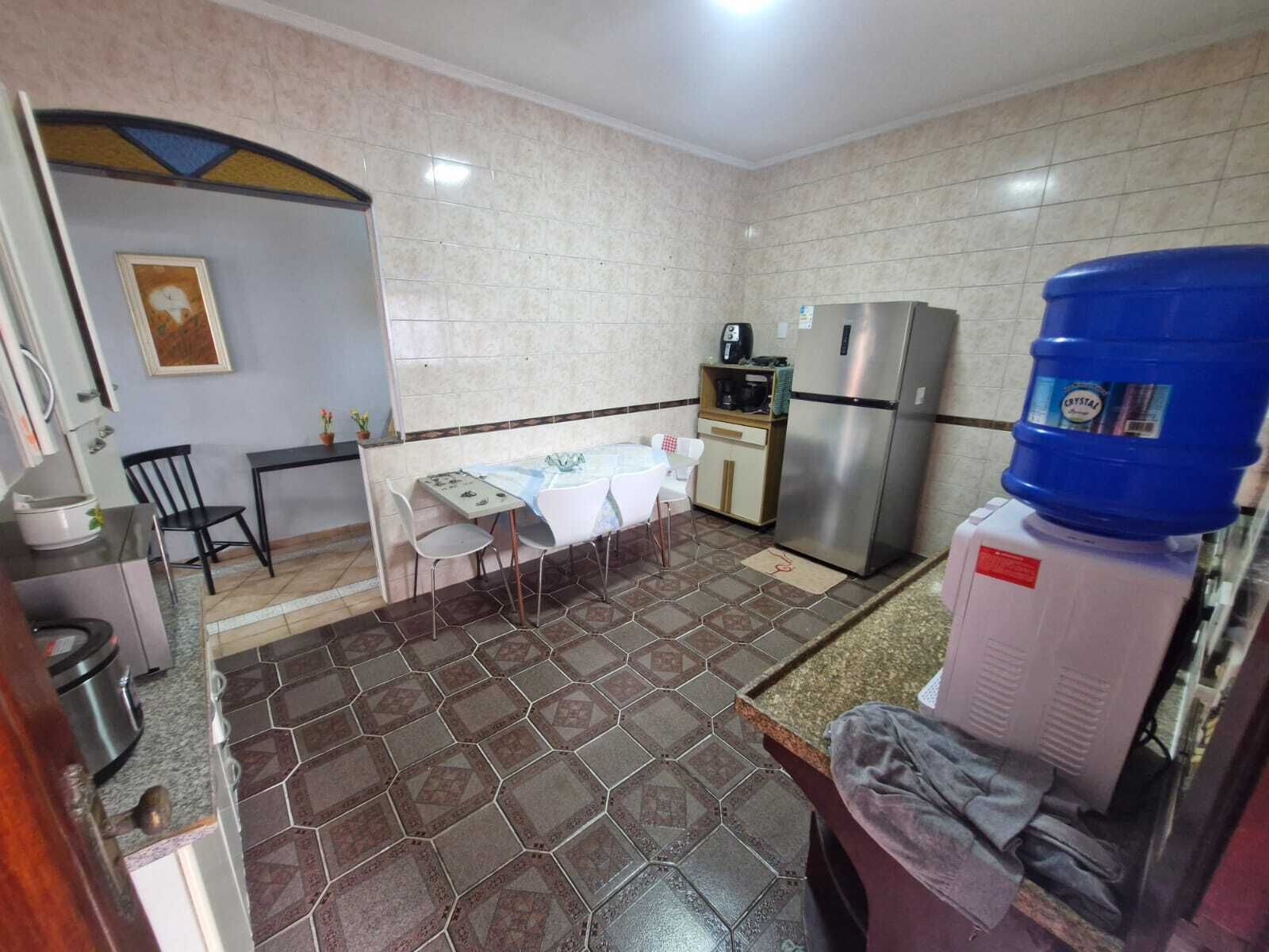 A compact kitchen with a dining table, chairs, a refrigerator, a water dispenser, and a tiled floor.