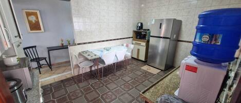 A compact kitchen with a dining table, chairs, a refrigerator, a water dispenser, and a tiled floor.