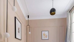Ett sovrum med en säng, sängbord, en hängande lampa och ett fönster med gardiner.