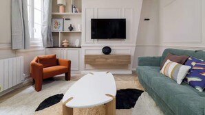 Ett vardagsrum med en soffa, fåtölj, soffbord, TV och hyllor med dekorativa föremål.