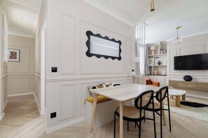 Ein modernes Wohnzimmer mit Flachbildfernseher, einem Essbereich mit Tisch und Stühlen sowie einer Küchenzeile mit Mikrowelle.