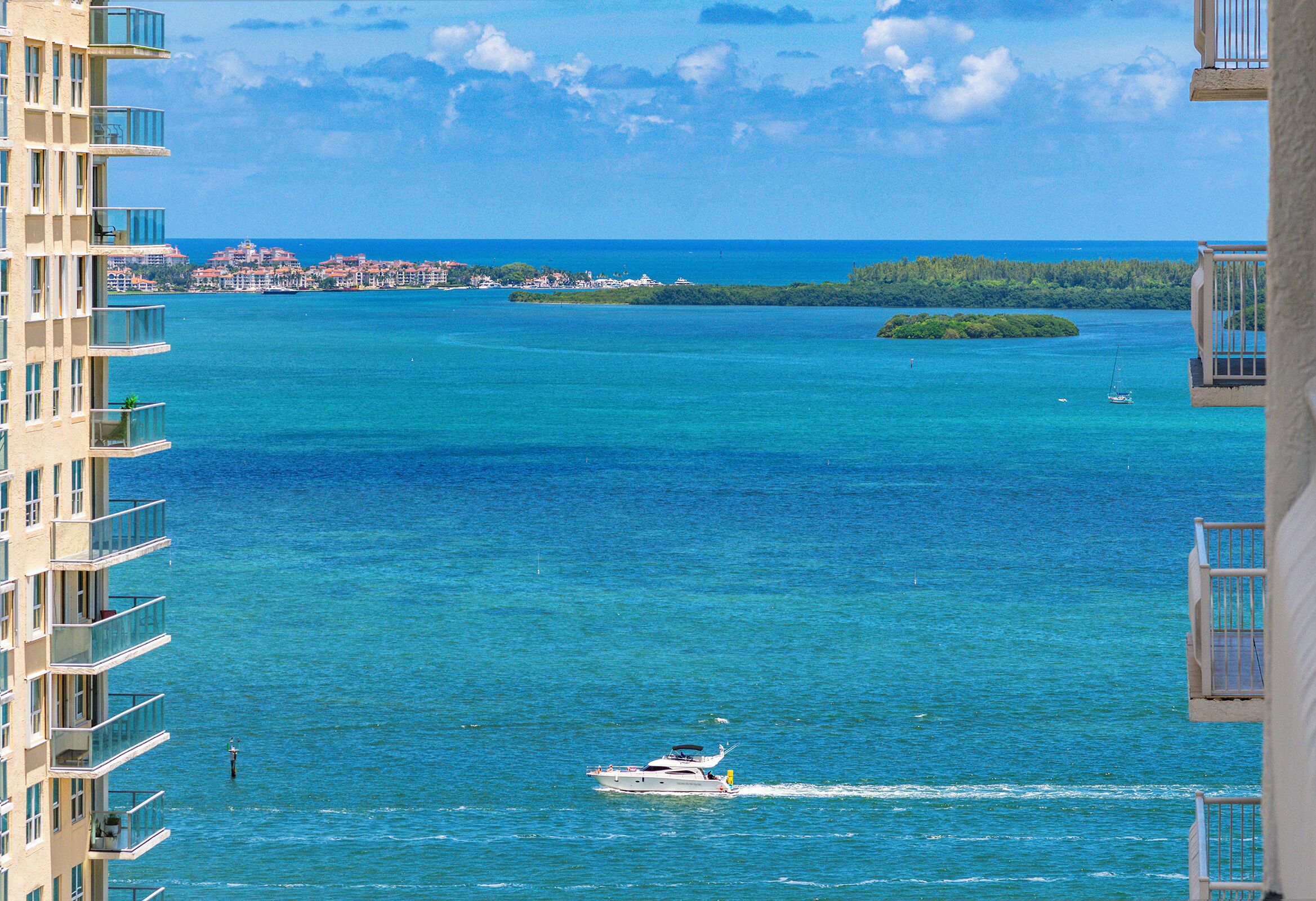 A waterfront view with a boat, buildings, and a distant island.