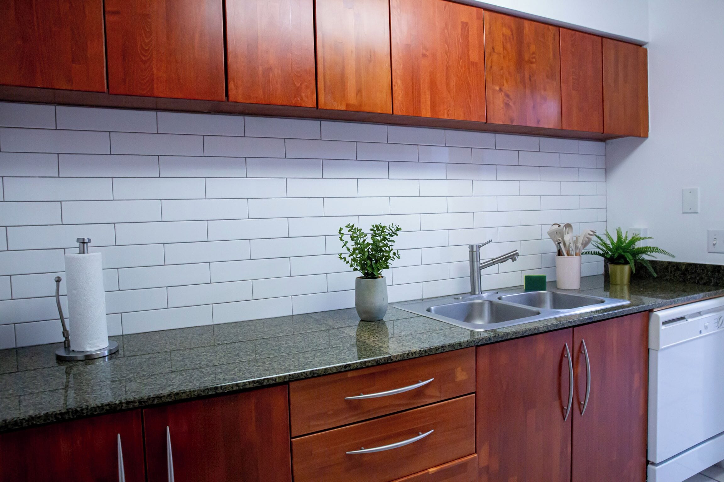 A kitchen with wooden cabinets, a granite countertop, a stainless steel sink, and a dishwasher.