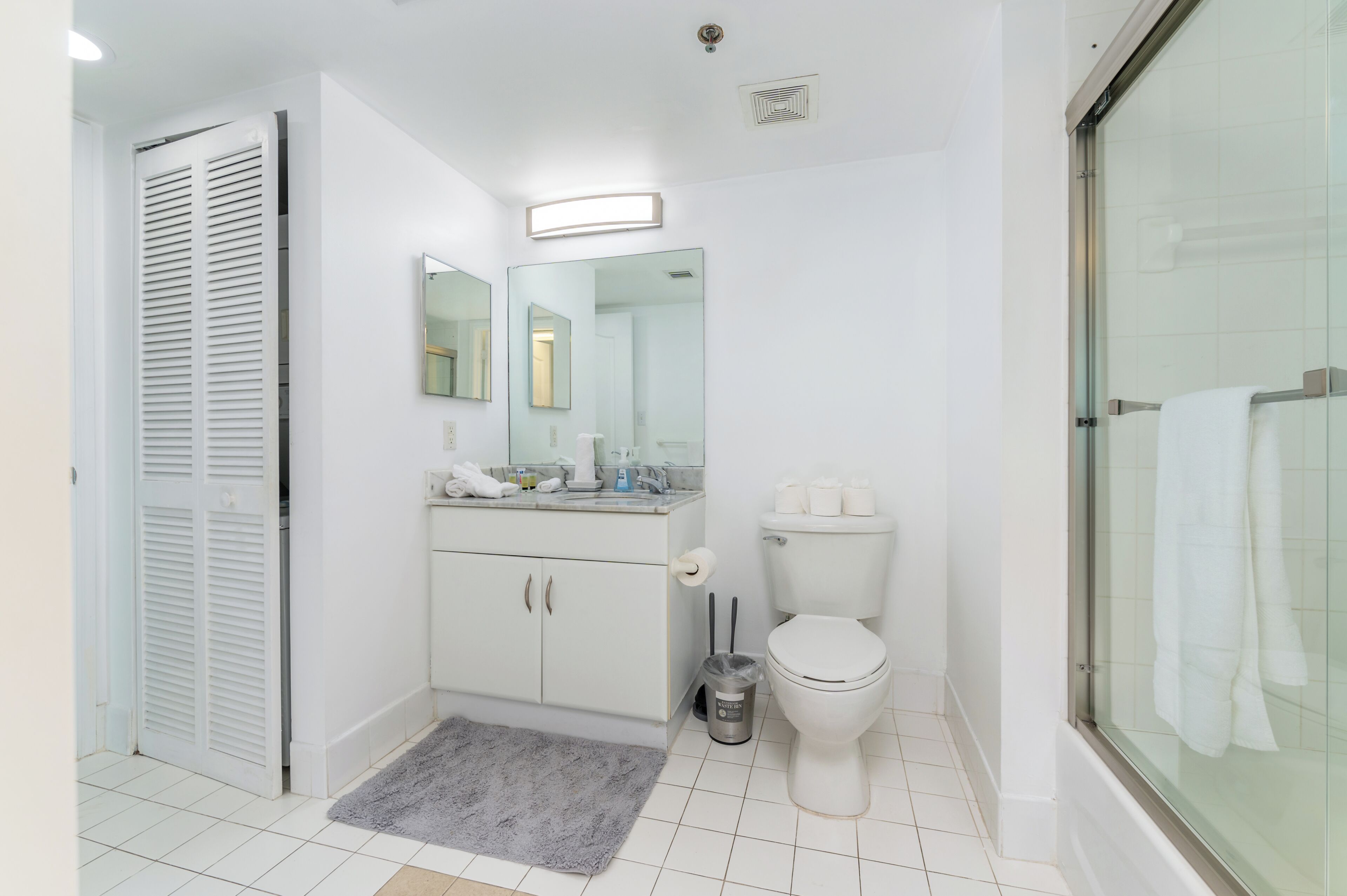 A bathroom with a toilet, sink, mirror, and shower.