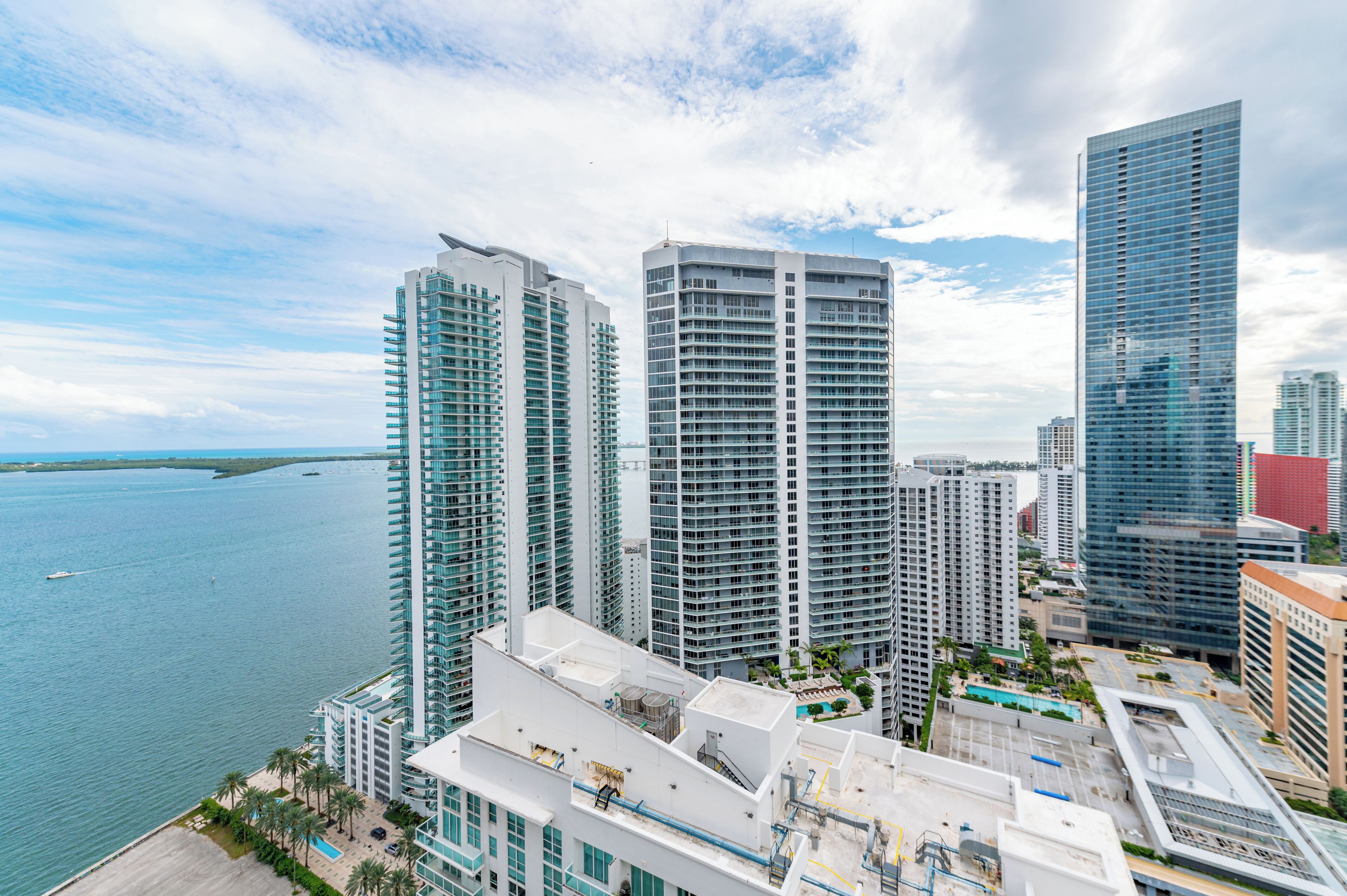 A high-rise building complex with multiple residential towers, a swimming pool, and a marina in the background.