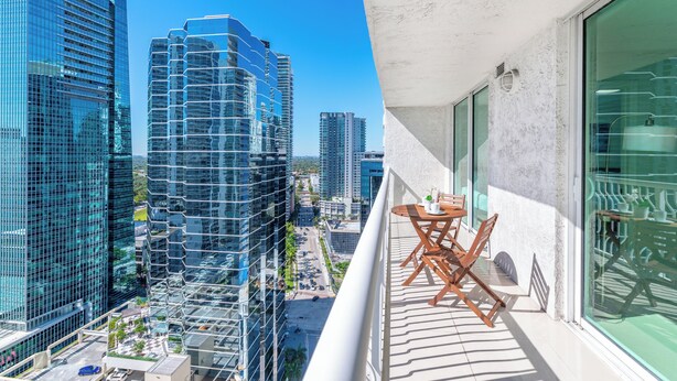Ein Balkon mit Tisch und Stühlen, mit Blick auf eine Skyline moderner Hochhäuser.