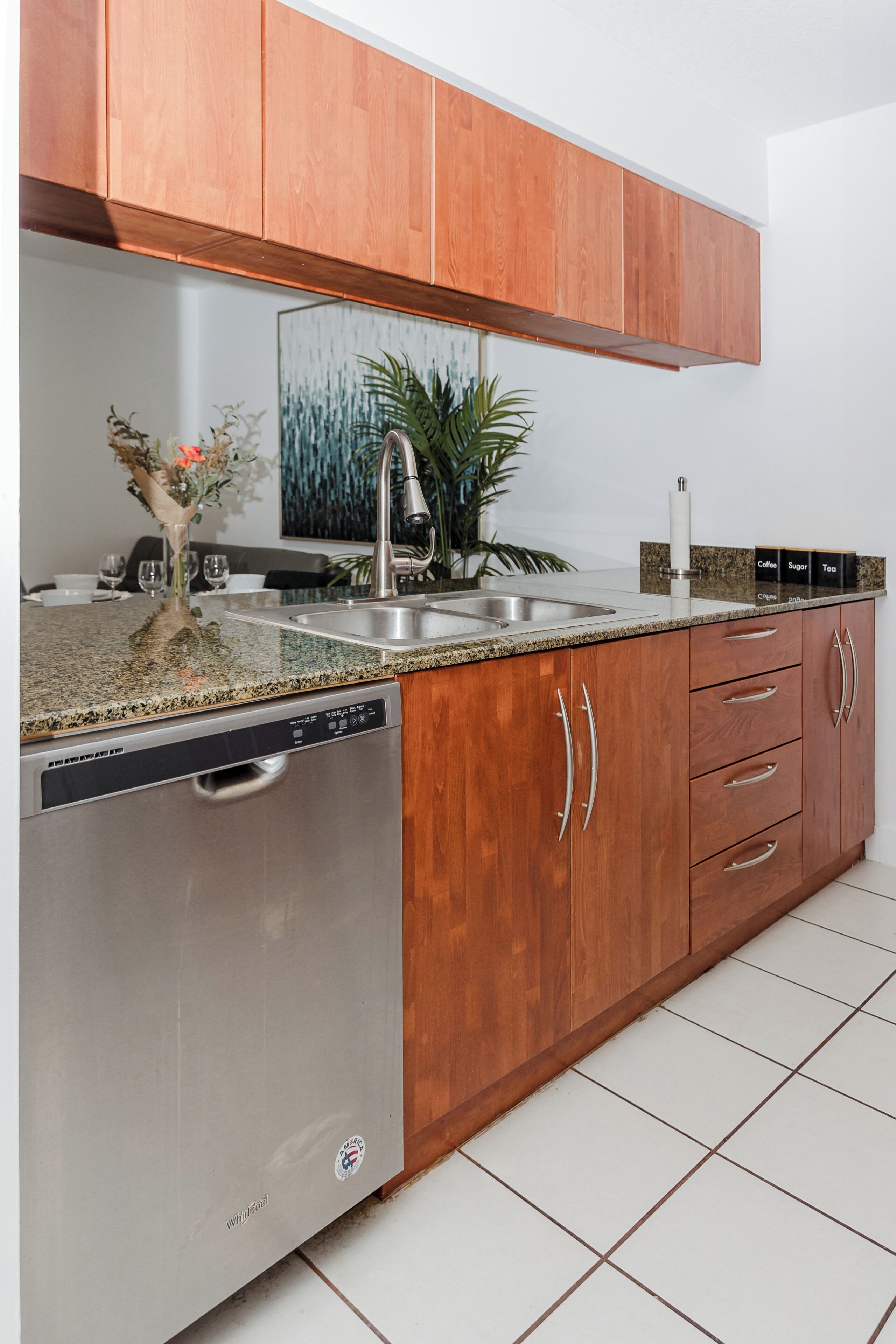 A kitchen with wooden cabinets, a stainless steel dishwasher, a granite countertop, and a sink.