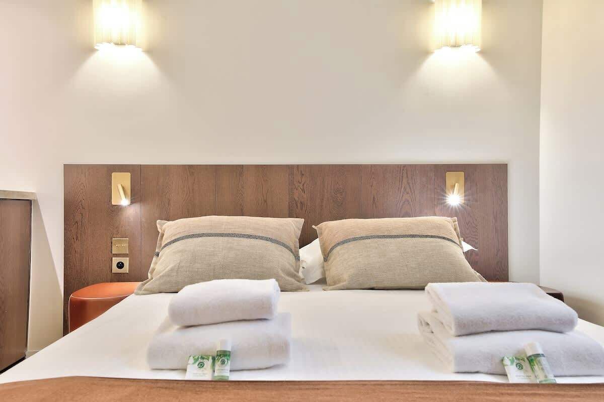 Une chambre d’hôtel avec une tête de lit en bois, deux lampes de chevet, une table de chevet et des serviettes soigneusement pliées.