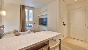Ett modernt hotellrum med en stor säng, ett matbord, en TV som är monterad på väggen och en garderob.