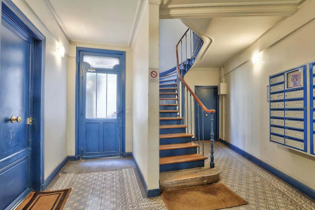 En hall med en blå dörr, en trappa med ett räcke och en vägg med arkivskåp.