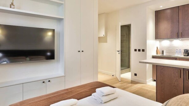 Ett modernt hotellrum med en platt-TV, en säng i trä, ett litet pentry och en rymlig klädkammare.