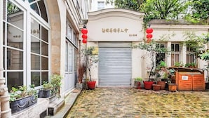 Une cour dallée de pierres, agrémentée de plantes en pot et fermée par un portail métallique.