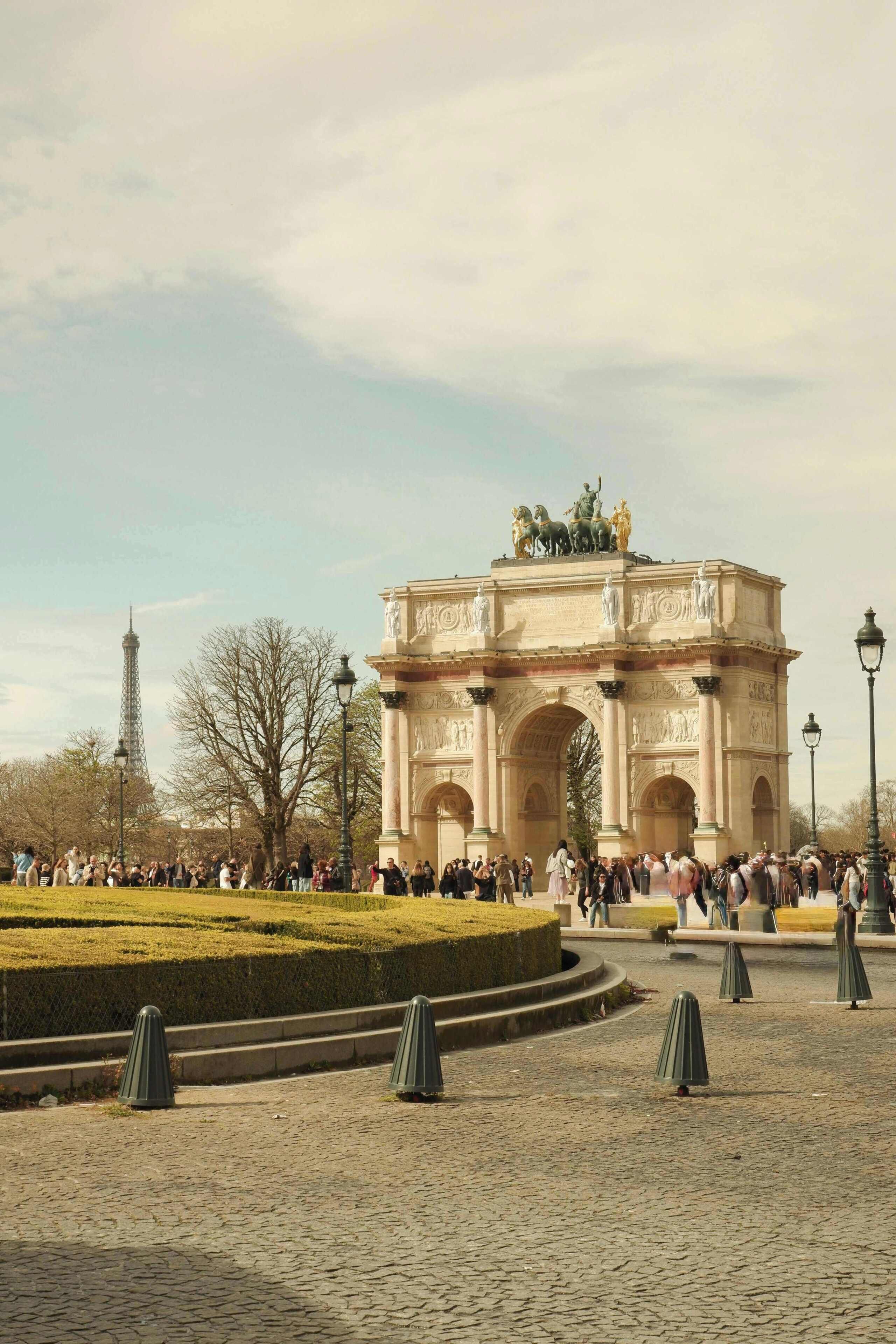 A large, ornate archway with statues, surrounded by a cobblestone plaza and a crowd of people.