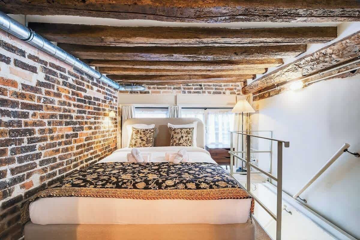Ein schmaler Raum mit einem Bett, einer Ziegelwand und freiliegenden Holzbalken.