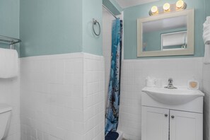 Un baño con ducha, un lavabo con espejo y un perchero para toallas.