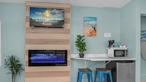 A kitchen with a flat-screen TV, a microwave, a refrigerator, and two blue stools. - Cozy 2 Queen Bed Studio in Sunny Fort Myers Beach (Fort Myers Beach)