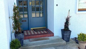 Una puerta azul con paneles de vidrio, un pequeño porche con escalones y dos macetas con plantas.
