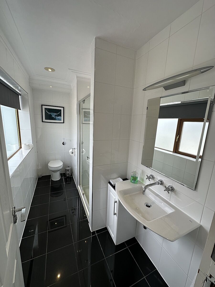 A modern bathroom with a toilet, sink, mirror, and a window.