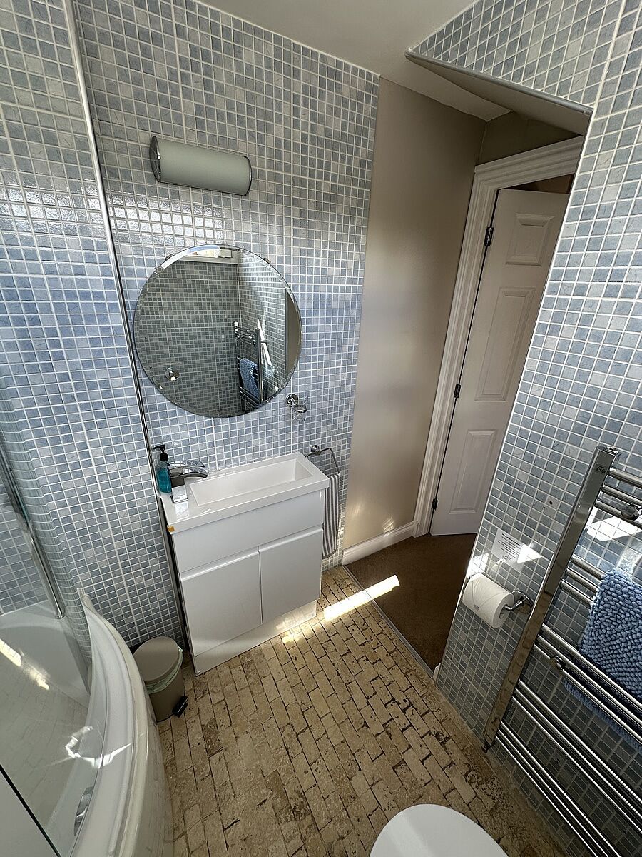 A bathroom with a tiled wall, a sink, a mirror, a toilet, and a shower area.