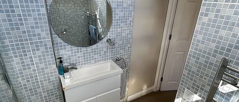 Une salle de bain avec un mur carrelé, un lavabo, un miroir, des toilettes et un espace douche.