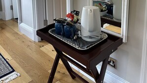 Habitación de hotel con un espejo grande, una mesita con cafetera y una cama con almohada roja.