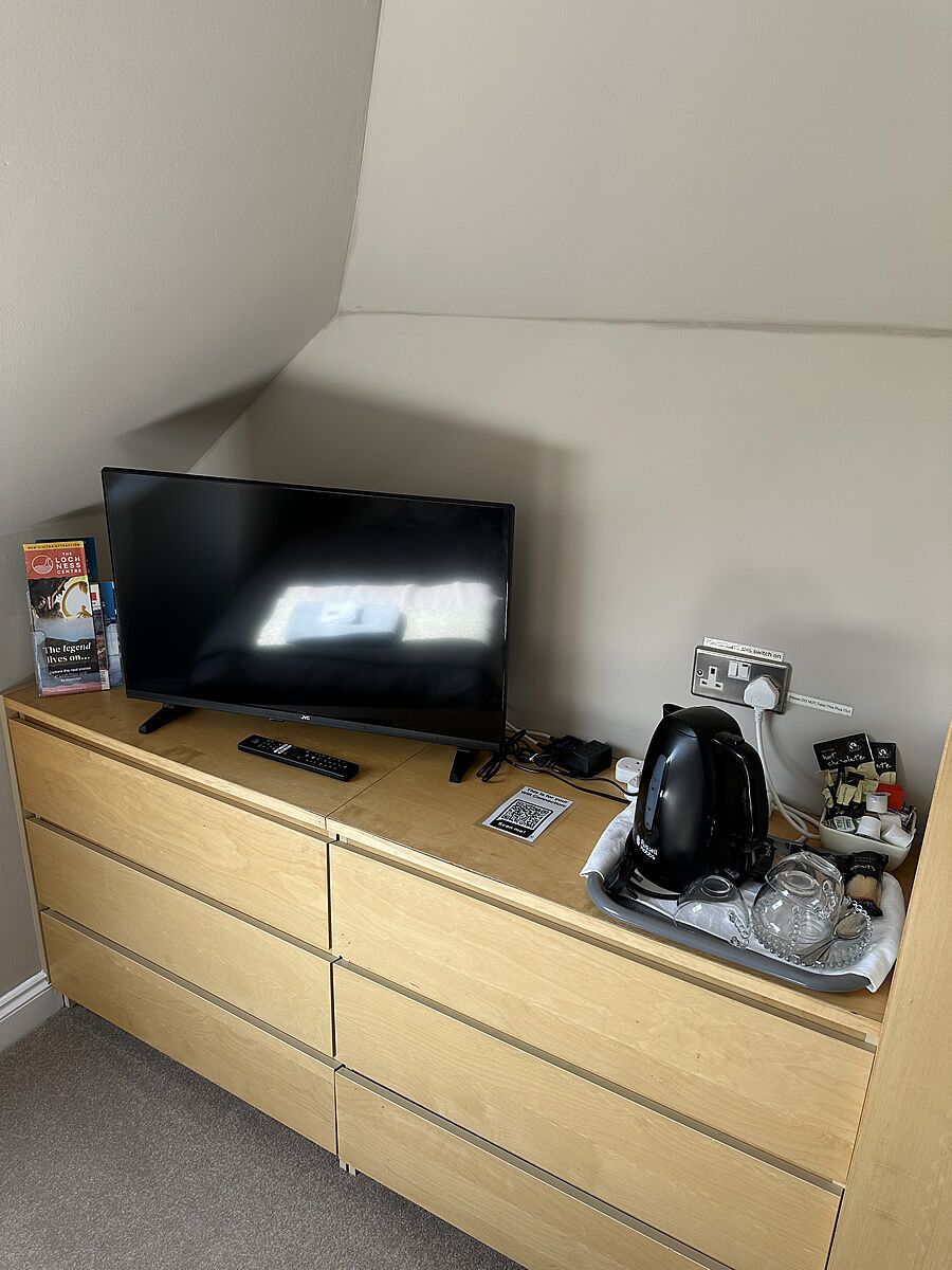 Ein Fernseher auf einer Holzkommode, eine Fernbedienung, eine Kaffeemaschine und ein Tablett mit Gläsern.