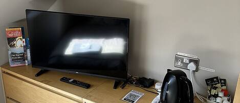 Ein Fernseher auf einer Holzkommode, eine Fernbedienung, eine Kaffeemaschine und ein Tablett mit Gläsern.