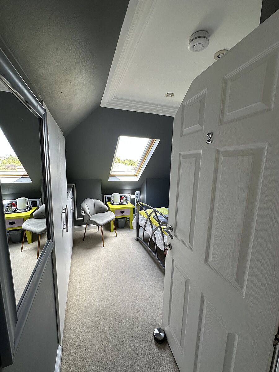 A room with a skylight, a bed, two chairs, a desk, and a door.