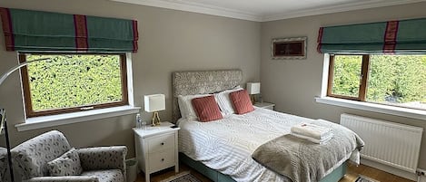 Un dormitorio con cama, mesitas de noche, una silla, ventana y radiador.