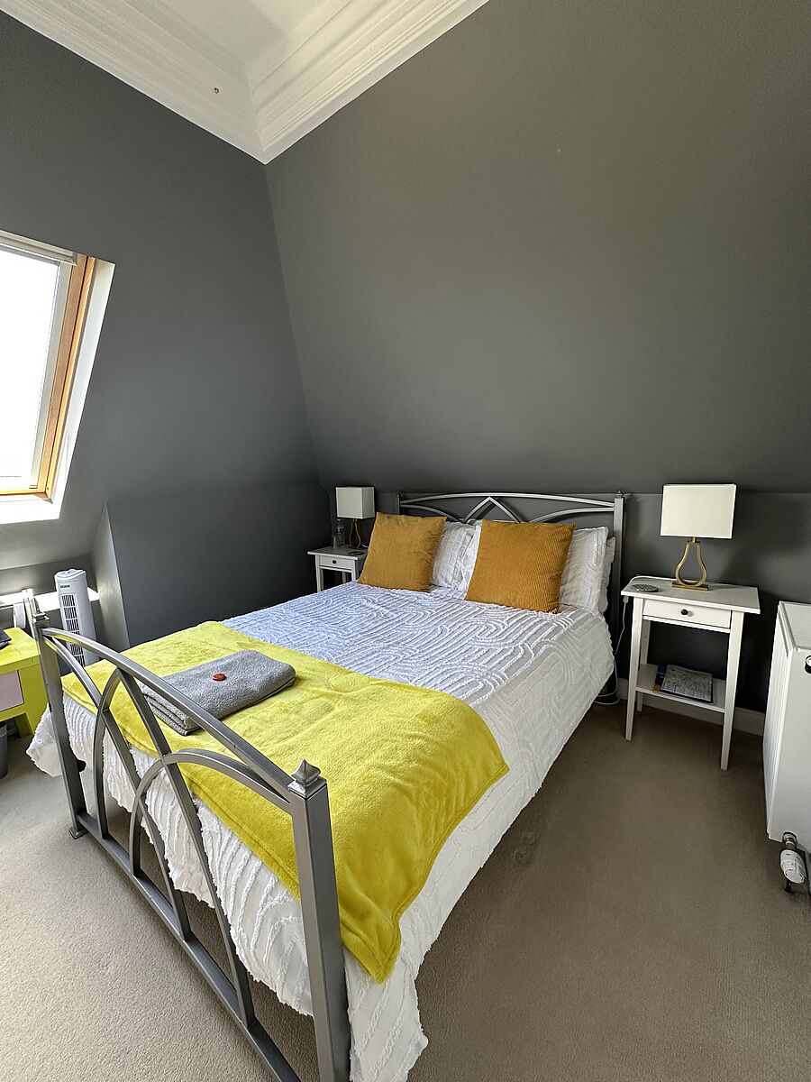 A bedroom with a bed, two bedside tables, a window, and a wheelchair.