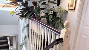 Una escalera de madera blanca con barandilla, un espejo en la pared y una planta en el rellano.