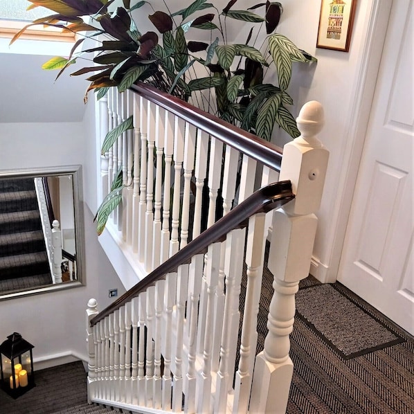 A white wooden staircase with a railing, a mirror on the wall, and a potted plant on the landing.