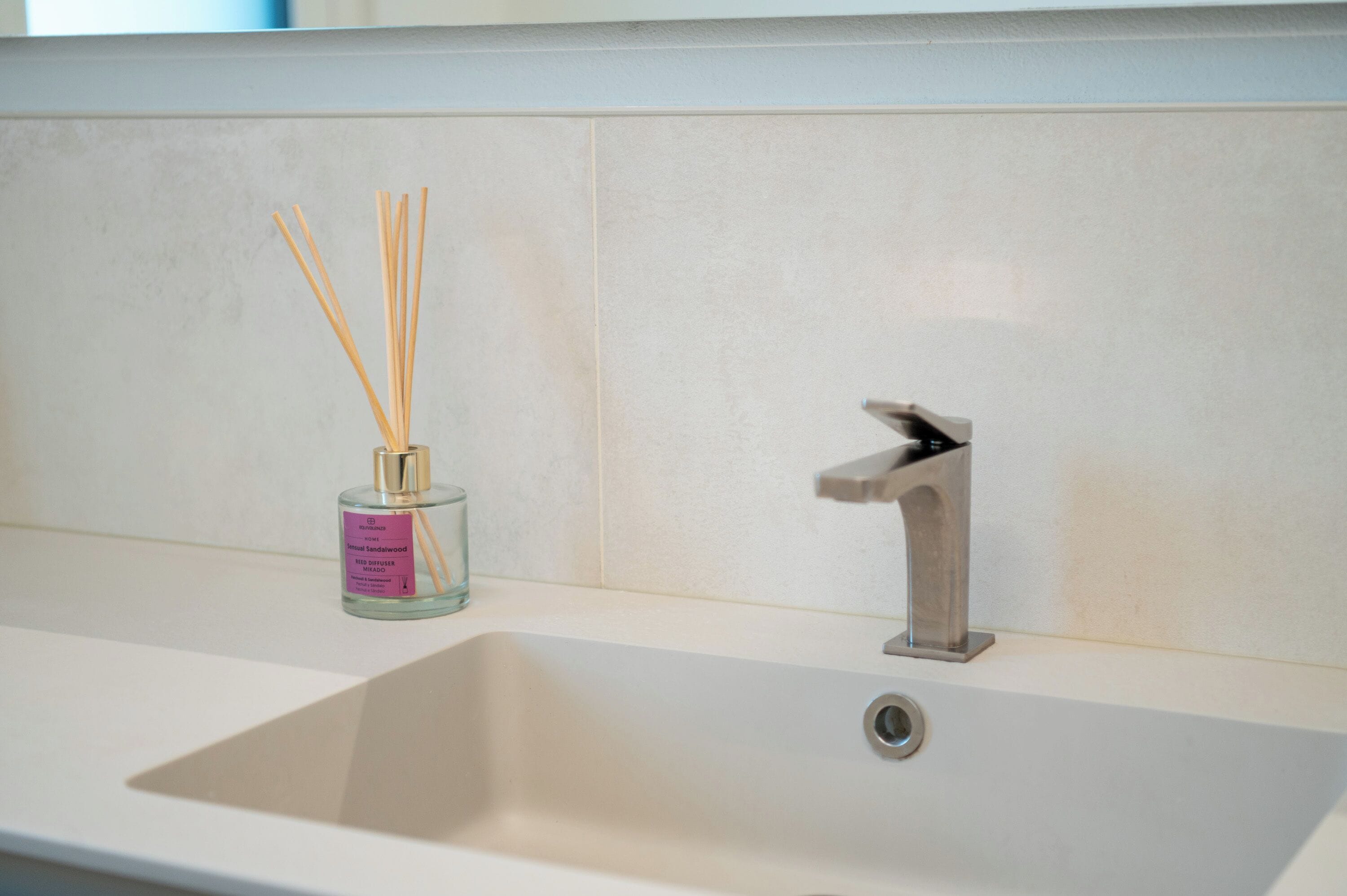 A bathroom with a white sink, a modern faucet, and a glass bottle with reed sticks.