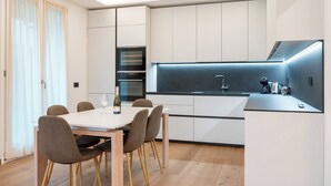 Een moderne keuken met een eethoek, voorzien van een inbouwoven, een roestvrijstalen afzuigkap en een fles wijn op tafel.