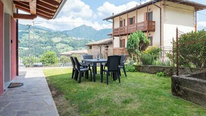 Een terras met een tafel en stoelen, een gebouw met balkon, en een bergachtig landschap op de achtergrond.