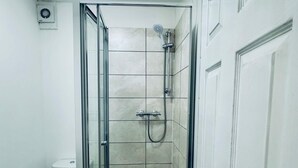 Ein kleiner, abgeschlossener Duschbereich mit Glastür, Toilette und Wandlüfter.