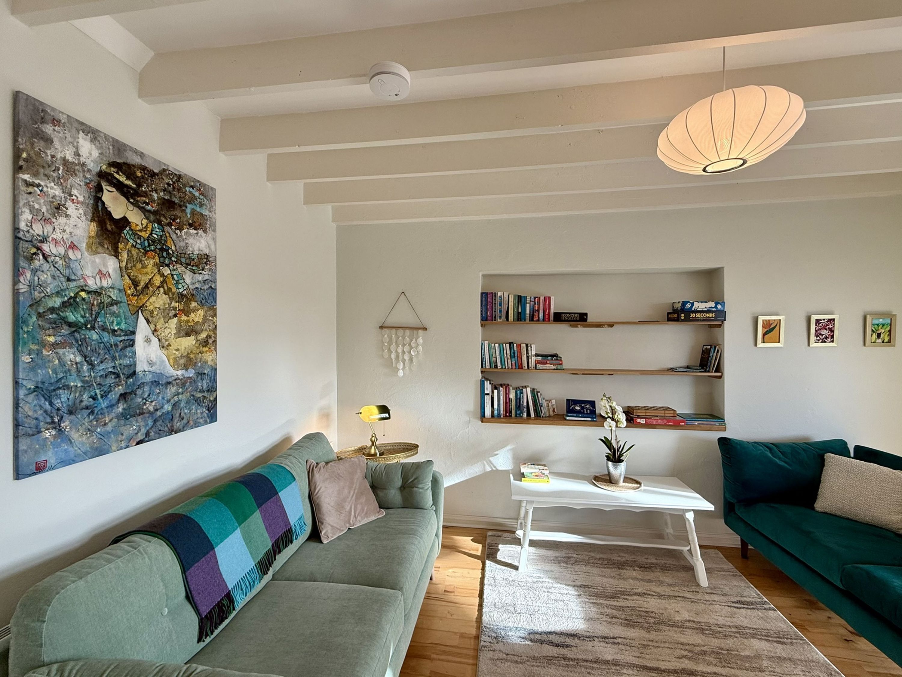 A living room with a green sofa, a white coffee table, a bookshelf, and a hanging light fixture.