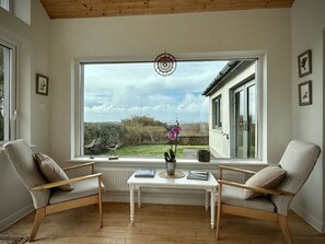 Ein Zimmer mit einem großen Fenster, zwei Stühlen, einem kleinen Tisch und einem Traumfänger.