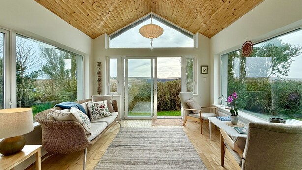 A spacious room with a high wooden ceiling, a large window, a sofa, a chair, and a table with a vase of flowers. - Cottage 498 - Cleggan - sleeps 9 guests  in 4 bedrooms (Cleggan)