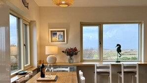 A dining area with a wooden table, white chairs, a vase with flowers, a lamp, and a seahorse decoration. - Cottage 498 - Cleggan - sleeps 9 guests  in 4 bedrooms (Cleggan)