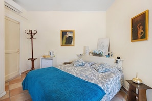 Ein Schlafzimmer mit einem Bett, einem Kleiderständer, einem kleinen Schreibtisch und einem Wandbild.