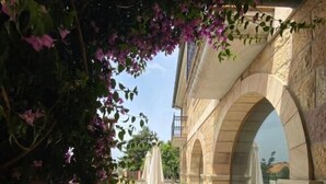 Un pati exterior amb mur de pedra, finestres d'arc i mobles blancs per a l'exterior.