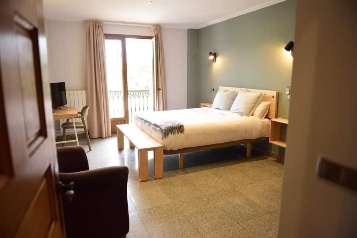 Un dormitorio con cama, escritorio, silla, banca y balcón.